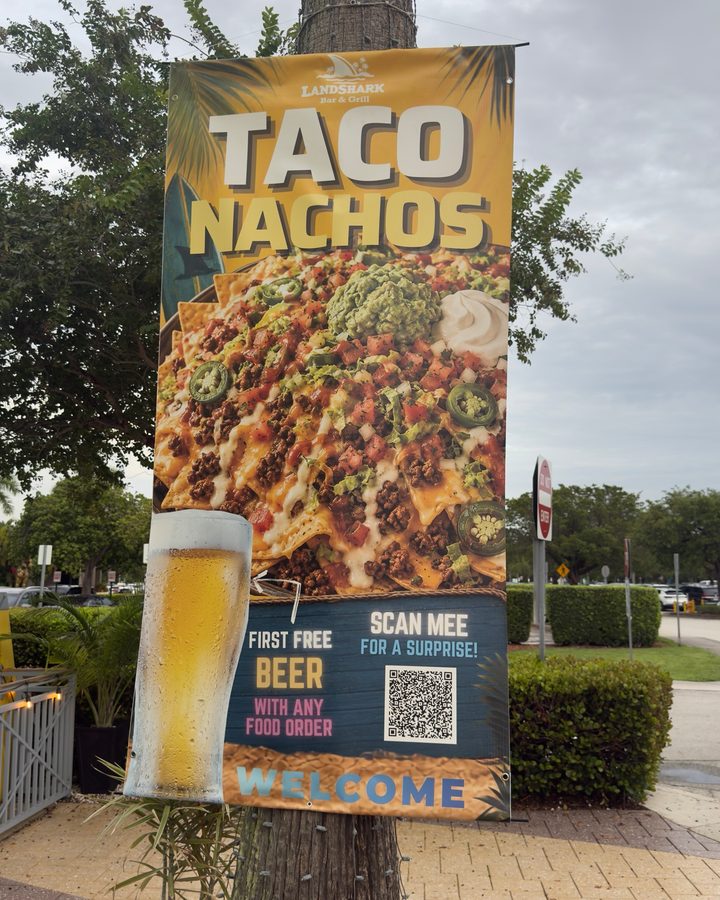 A banner hanging on a palm tree, on the street